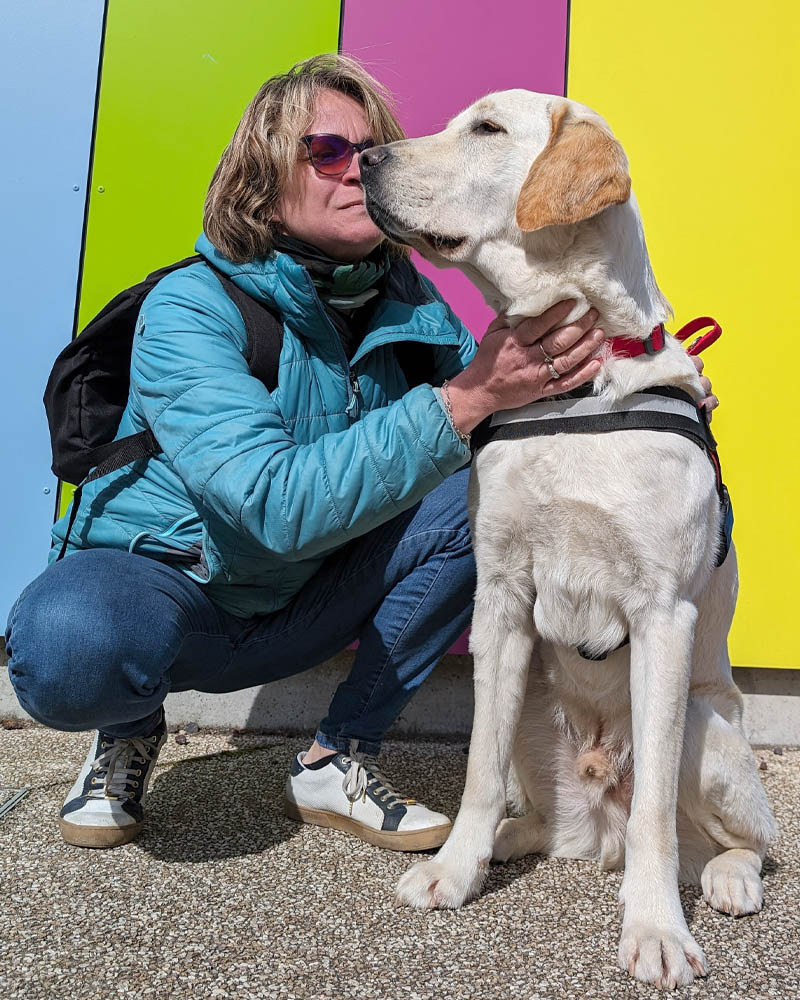 Story et Séverine Dejeux, accroupis l'un à côté de l'autre devant un décor mural aux couleurs vives. Sandrine caresse le poitrail de Story.