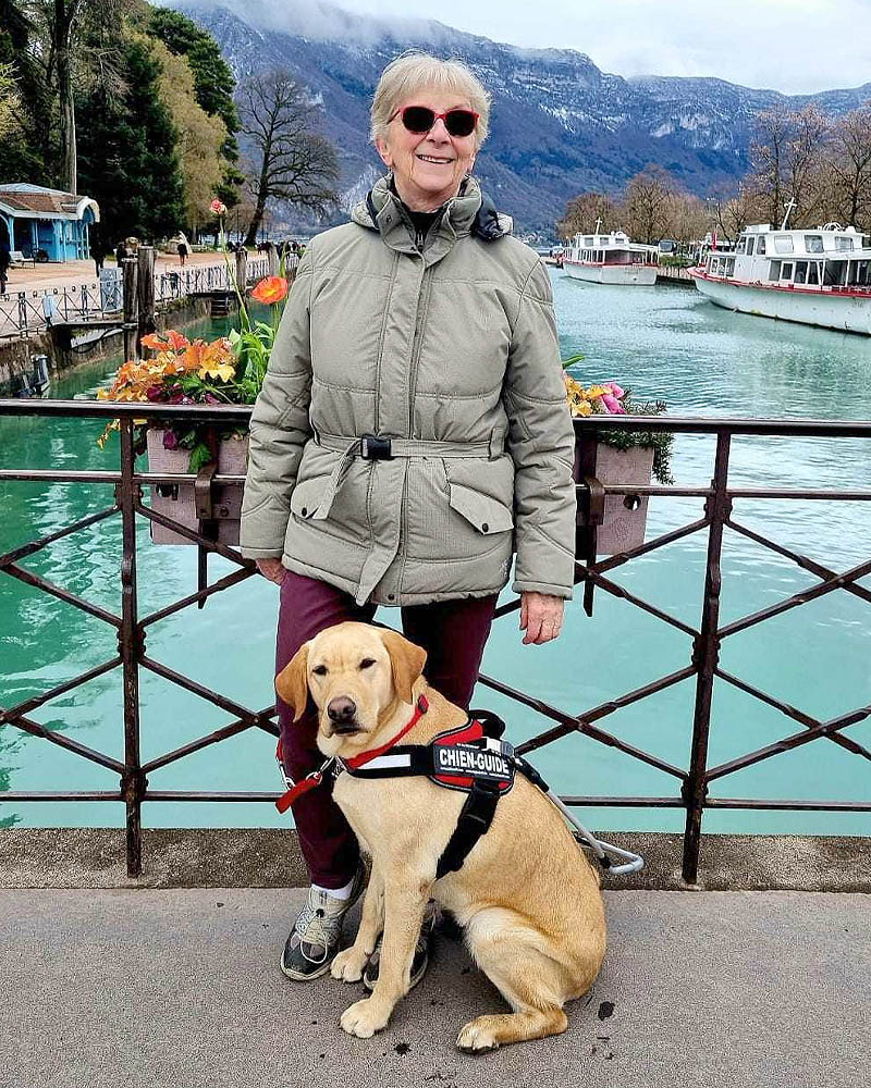 Agnès Faure et Tismi devant le canal d'Annecy. Agnès est appuyée à la balustrade, Tismi assis à ses pieds.