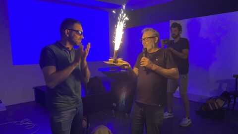 Président et VP lors des 40 ans de l'association, sur un fond bleu, tenant une bougie/torche. Ils sont tous deux habillés en noir.