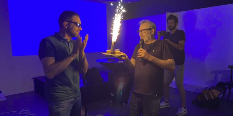 Président et VP lors des 40 ans de l'association, sur un fond bleu, tenant une bougie/torche. Ils sont tous deux habillés en noir.