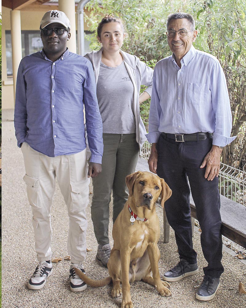 De gauche à droite : Souleyman, Adeline Scerri et Lucien Chaline. Devant eux, assis, Ubble fixe l'objectif. Photo prise devant le bâtiment de l'école à Misérieux.