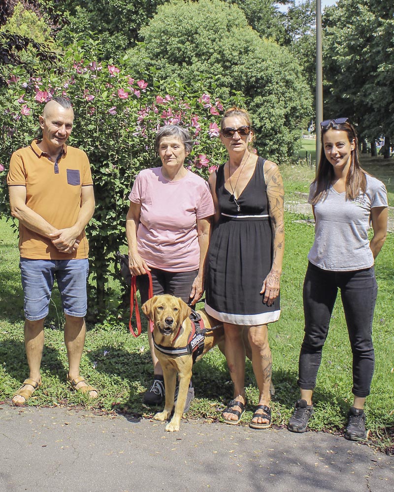 Remise de Umpa à Misérieux, sur fond verdoyant et fleuri. Debouts de gauche à droite : Philippe Bazoge, Nathalie Alonso, Nadine Bazoge et Estelle Moreno Gonzalez. Debout devant Nathalie, Umpa en laisse et équipé de son harnais de chien guide.