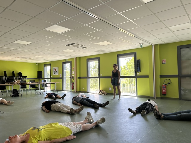 Les participants de l'atelier sont allongés dans la salle de formation pour un moment de respiration et d'ancrage au sol tandis que la chorégraphe, debout, donne des indications