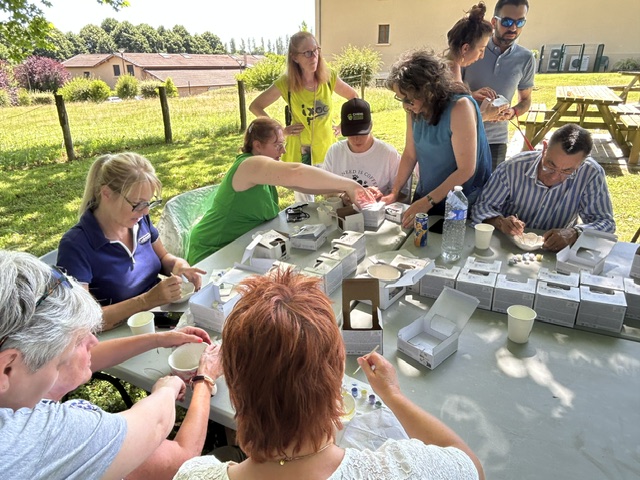 Un autre angle de nos participants en train de peindre, l'ombre des arbres. On voit le bâtiment administratif en arrière plan, de l'herbe et une table de pique-nique.